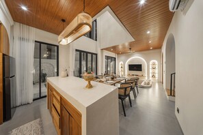 Una cucina moderna con isola centrale, soffitto in legno e zona pranzo con sedie e tavolo.
