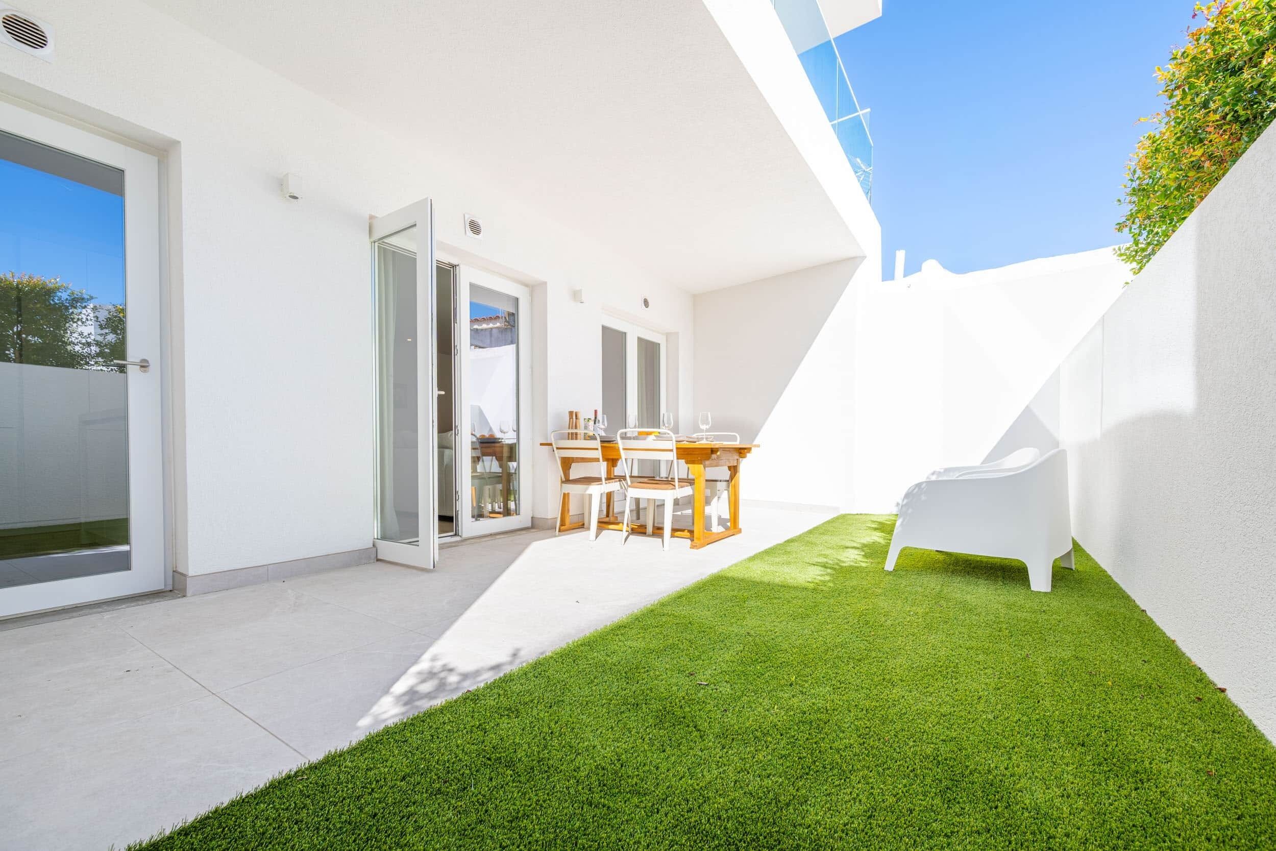 A modern outdoor patio with a dining area, a white chair, and a small lawn.