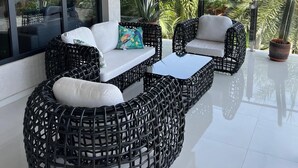 A modern outdoor seating area with wicker furniture and a glass table, overlooking a lush garden and palm trees. - Tropical Luxury Oasis: 2 King Beds, 2.5 Baths, 3 Min Drive to Palm Beach (Noord)