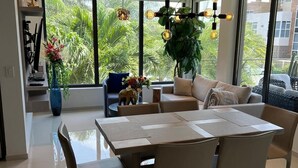 A modern dining area with a large table and chairs, a sofa, and a potted plant. - Tropical Luxury Oasis: 2 King Beds, 2.5 Baths, 3 Min Drive to Palm Beach (Noord)