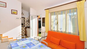 A cozy room with a dining table, orange sofa, and a window with yellow curtains. - Nice apartment in villa for 5 guests with A/C, TV, terrace and pets allowed (San Michele Al Tagliamento)