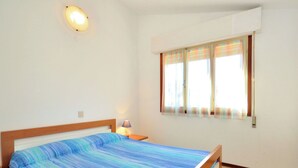 A bedroom with a bed, a nightstand, a lamp, a window with curtains, and a wall-mounted light fixture. - Nice apartment in villa for 5 guests with A/C, TV, terrace and pets allowed (San Michele Al Tagliamento)