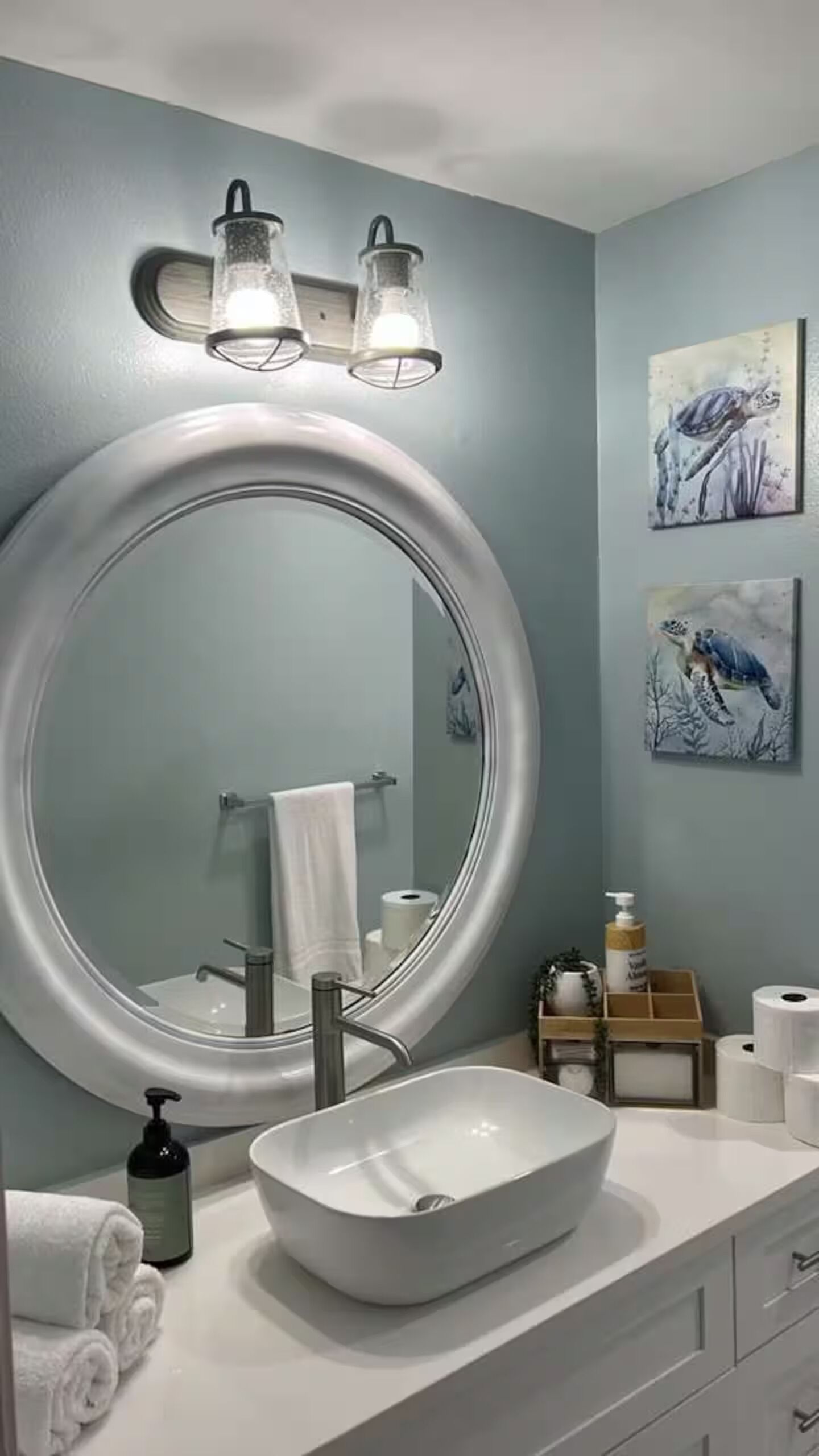 A bathroom with a large round mirror, a vessel sink, and two wall-mounted lights.