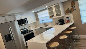 A modern kitchen with white cabinetry, stainless steel appliances, a large island with stools, and a decorative wall piece. - Spa Beach Retreat • Sleeps 10 • 8 min to Beach (Englewood)