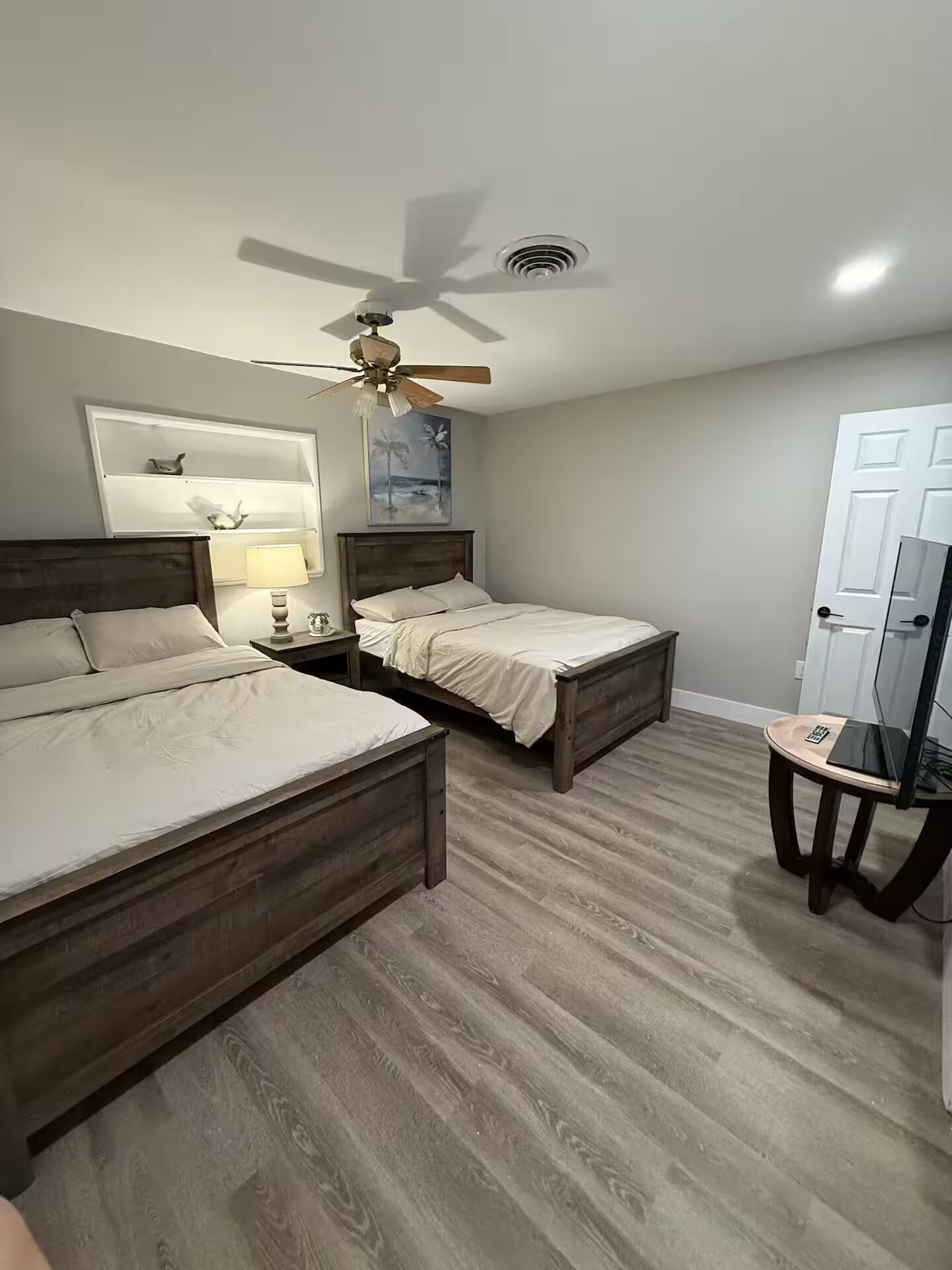 A bedroom with two wooden beds, a ceiling fan, a painting, and a television on a small table.