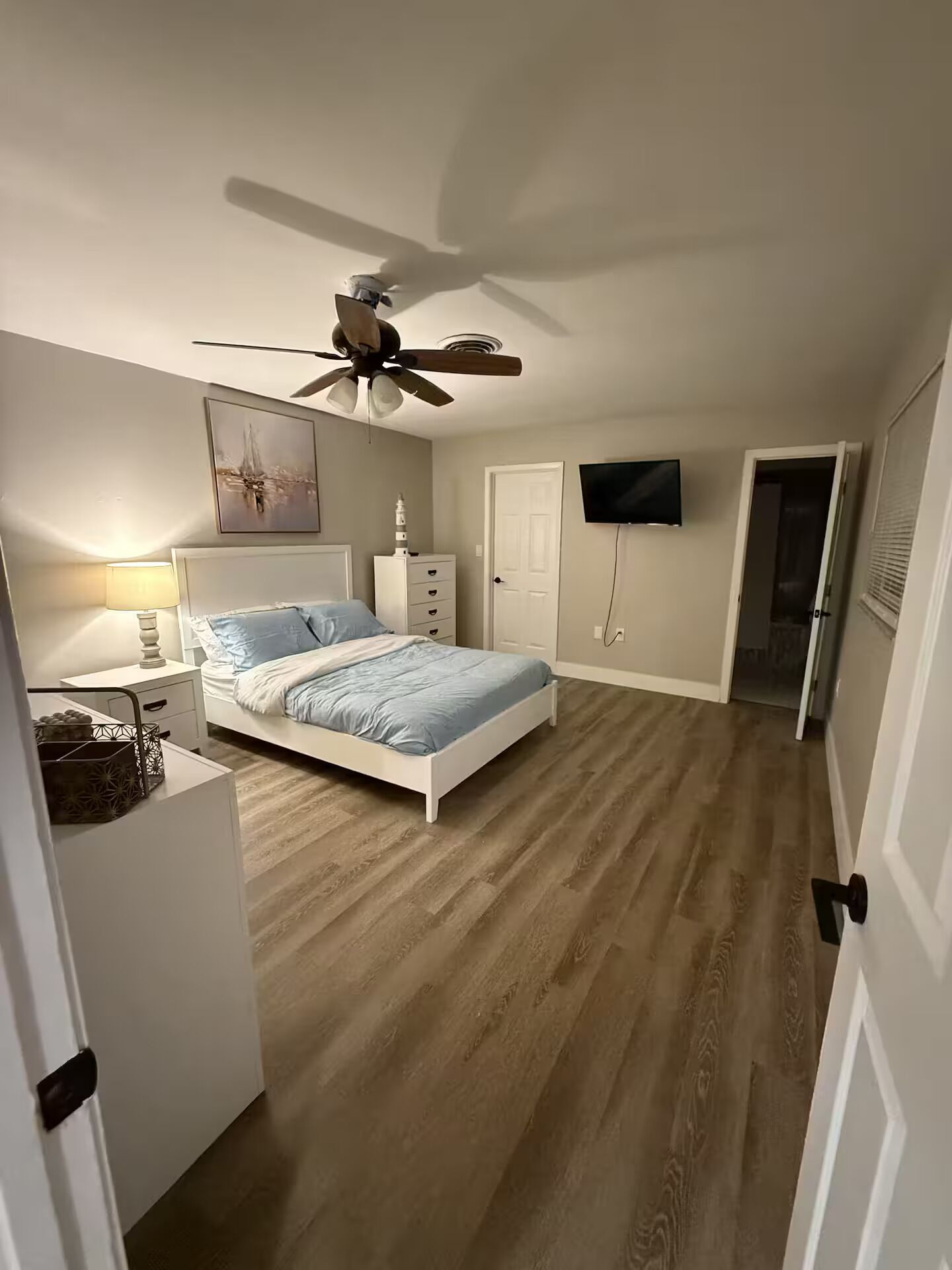 A bedroom with a bed, a ceiling fan, a TV, and a door leading to another room.