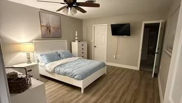 A bedroom with a bed, a ceiling fan, a TV, and a door leading to another room.