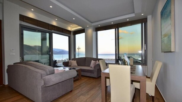 A modern living room with a large window, a sofa, a dining table, and chairs. - Gonis Grand Luxury Suite (Kantanos-Selino)