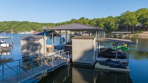 A dock with a covered seating area, a small building, and a kayak. - Spacious Lakefront Getaway with Dock in Quiet Cove (Lake Ozark)
