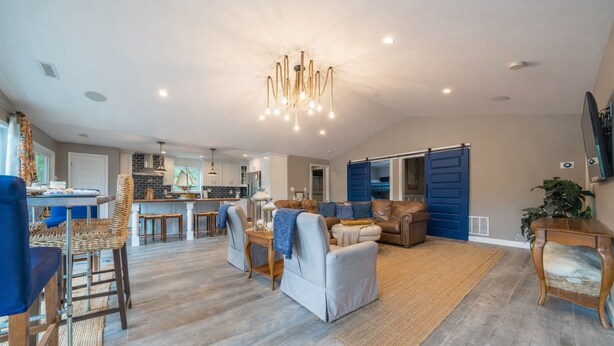 A spacious living area with a modern chandelier, a kitchen in the background, and a blue sliding door. - Spacious Lakefront Getaway with Dock in Quiet Cove (Lake Ozark)