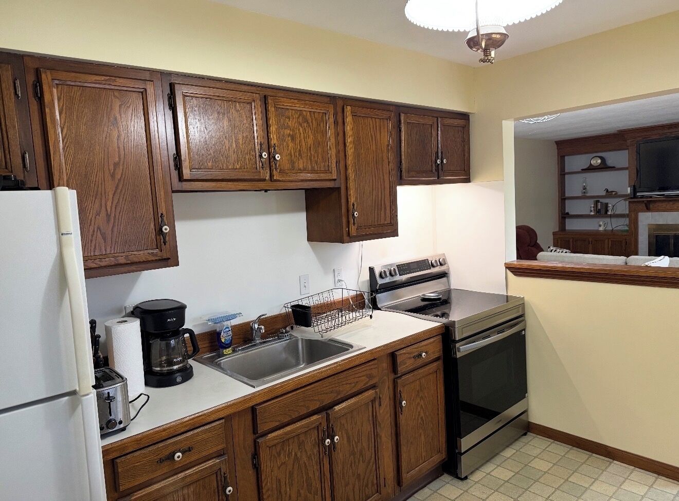 A kitchen with wooden cabinets, a refrigerator, a stove, and a coffee maker.