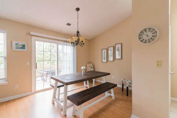 A dining area with a wooden table and bench, a chandelier, and a clock on the wall.