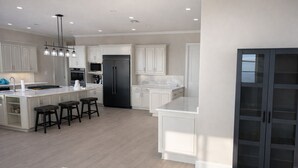 A modern kitchen with white cabinetry, a central island with stools, a built-in oven, and a refrigerator. - Spacious 6-bedroom house on lake with extra large kitchen and great swimming. (Corsicana)