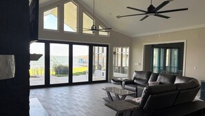 A spacious living room with a large sliding glass door leading to a balcony, a ceiling fan, and a leather sofa. - Spacious 6-bedroom house on lake with extra large kitchen and great swimming. (Corsicana)