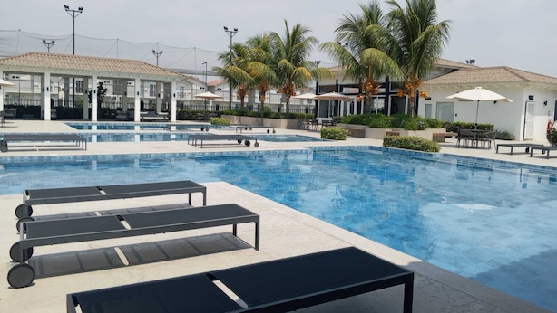 Ein Swimmingpool mit Liegestühlen, Palmen und einem Gebäude mit einem Ziegeldach.