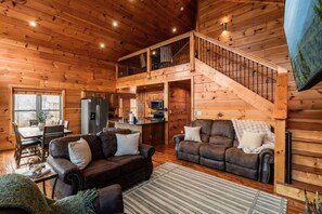 A cozy cabin interior with a dining area, two sofas, a kitchen, and a staircase. - VIEWS/Hot Tub/Fire Pit/Game Room/Daybed Swing - Three Bears Chalet (Gatlinburg)