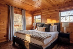 A wooden cabin bedroom with a bed, nightstands, and windows. - VIEWS/Hot Tub/Fire Pit/Game Room/Daybed Swing - Three Bears Chalet (Gatlinburg)