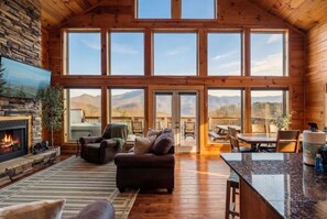 Un salón amplio con chimenea de piedra, ventanas grandes y vistas a montañas.