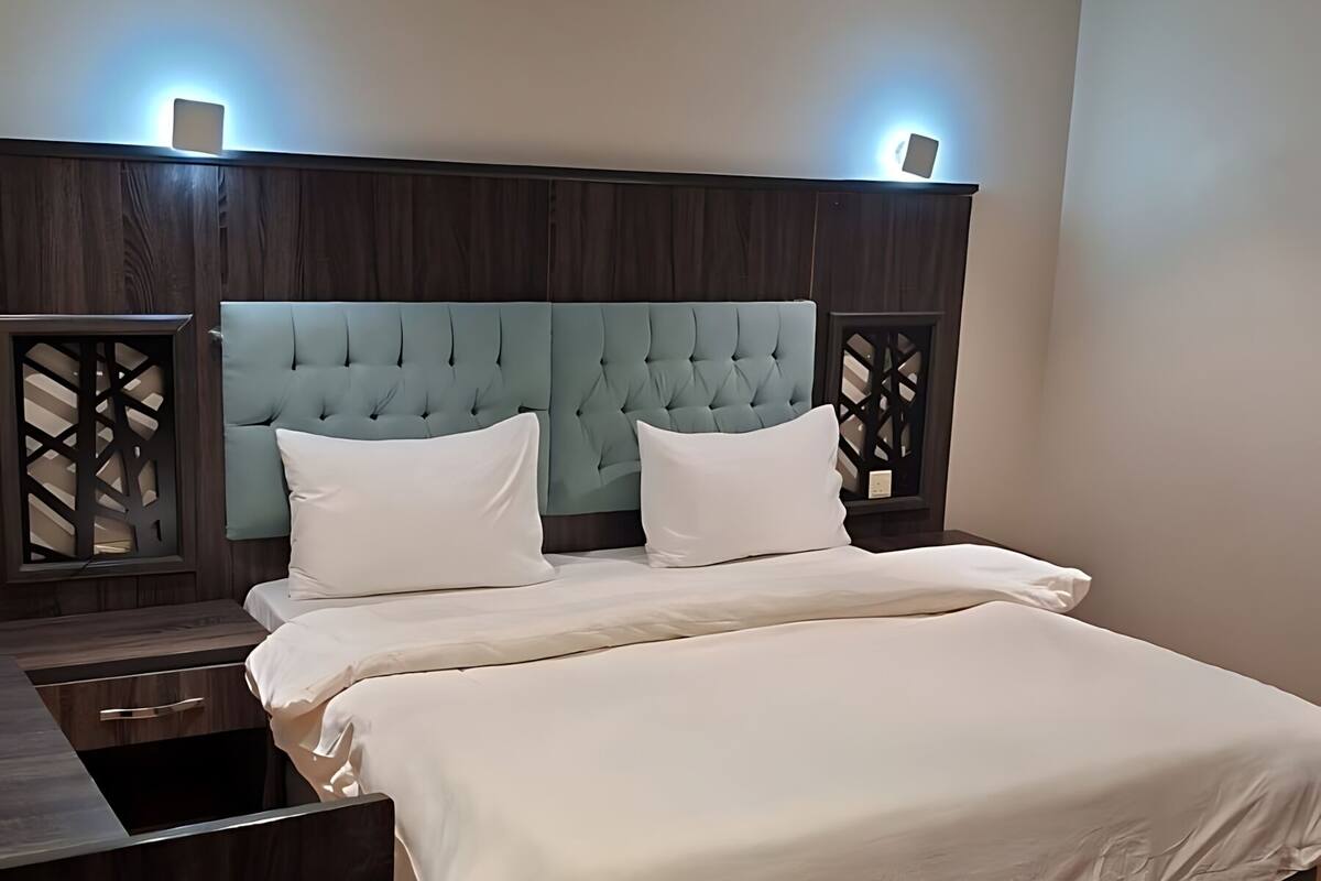 Un dormitorio moderno con una cabecera capitonada, una cama grande con ropa de cama blanca, una mesita de noche de madera y un escritorio empotrado.