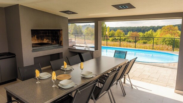 A modern dining area with a pool view, a fireplace, and a spacious table set for four. - Family-friendly hillside villa with pool, jacuzzi, sauna, terrace, and scenic Medvednica views. (Strmec Stubički)