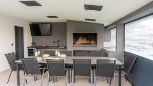 A modern dining area with a fireplace, a TV mounted on the wall, and a large window. - Family-friendly hillside villa with pool, jacuzzi, sauna, terrace, and scenic Medvednica views. (Strmec Stubički)
