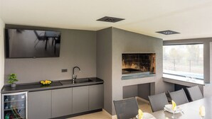 A modern kitchen with a flat-screen TV, a built-in grill, and a dining area with a table and chairs. - Family-friendly hillside villa with pool, jacuzzi, sauna, terrace, and scenic Medvednica views. (Strmec Stubički)