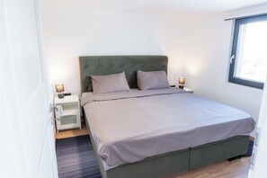 Una cama bien hecha con un cabecero verde, dos lámparas de noche y una ventana con vistas.