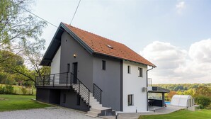 A modern two-story house with a grey exterior, a red-tiled roof, and a covered outdoor area. - Family-friendly hillside villa with pool, jacuzzi, sauna, terrace, and scenic Medvednica views. (Strmec Stubički)