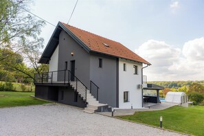Una casa moderna de dos pisos con fachada gris, techo de tejas rojas y un espacio exterior cubierto.