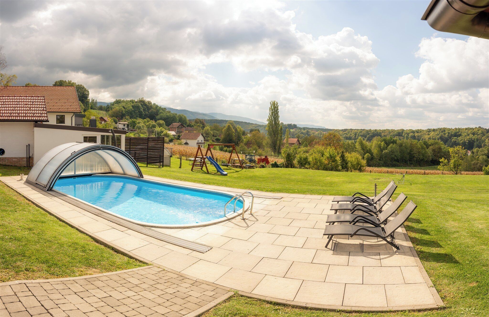 A swimming pool with a covered area, outdoor seating, and a view of a rural landscape with houses and trees.