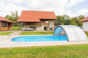 Ein Pool mit überdachtem Bereich, ein Steinhaus mit rotem Dach und eine Holzhütte mit Schornstein.