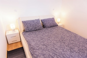 Ein ordentlich bezogenes Bett mit einem blumigen Überwurf und zwei passenden Kissen, begleitet von weißen Nachttischen mit Lampen.