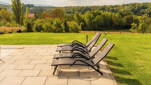 A row of black lounge chairs on a paved patio with a grassy lawn and trees in the background. - Villa in the Stubica region with wellness, jacuzzi, sauna, and pool for relaxation (Strmec Stubički)