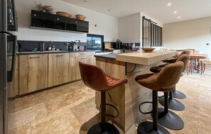 Eine moderne Küche mit Holzausbau, einer schwarzen Arbeitsplatte und einer großen Kochinsel mit Barhocker.