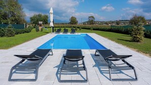 Una piscina con tres tumbonas y una sombrilla.