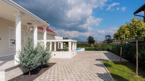 Una casa moderna con un porche cubierto, una piscina y un jardín bien cuidado.