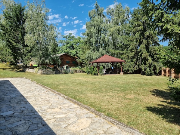 A stone pathway leading to a rustic wooden cabin with a red gazebo in a lush green setting. - Relax with jacuzzi, pool and authentic Slavonian charm (Požega)