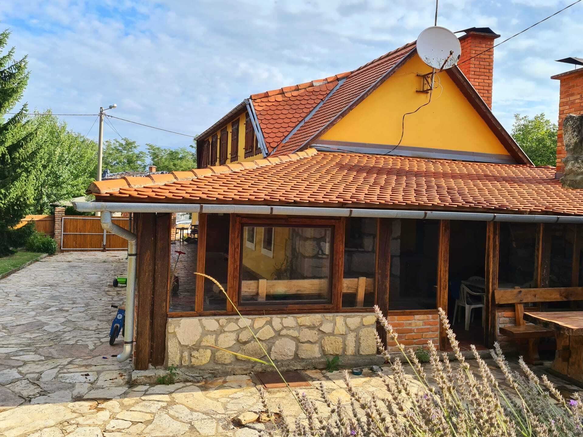 Una casa amarilla con techo de tejas, base de piedra y porche de madera.