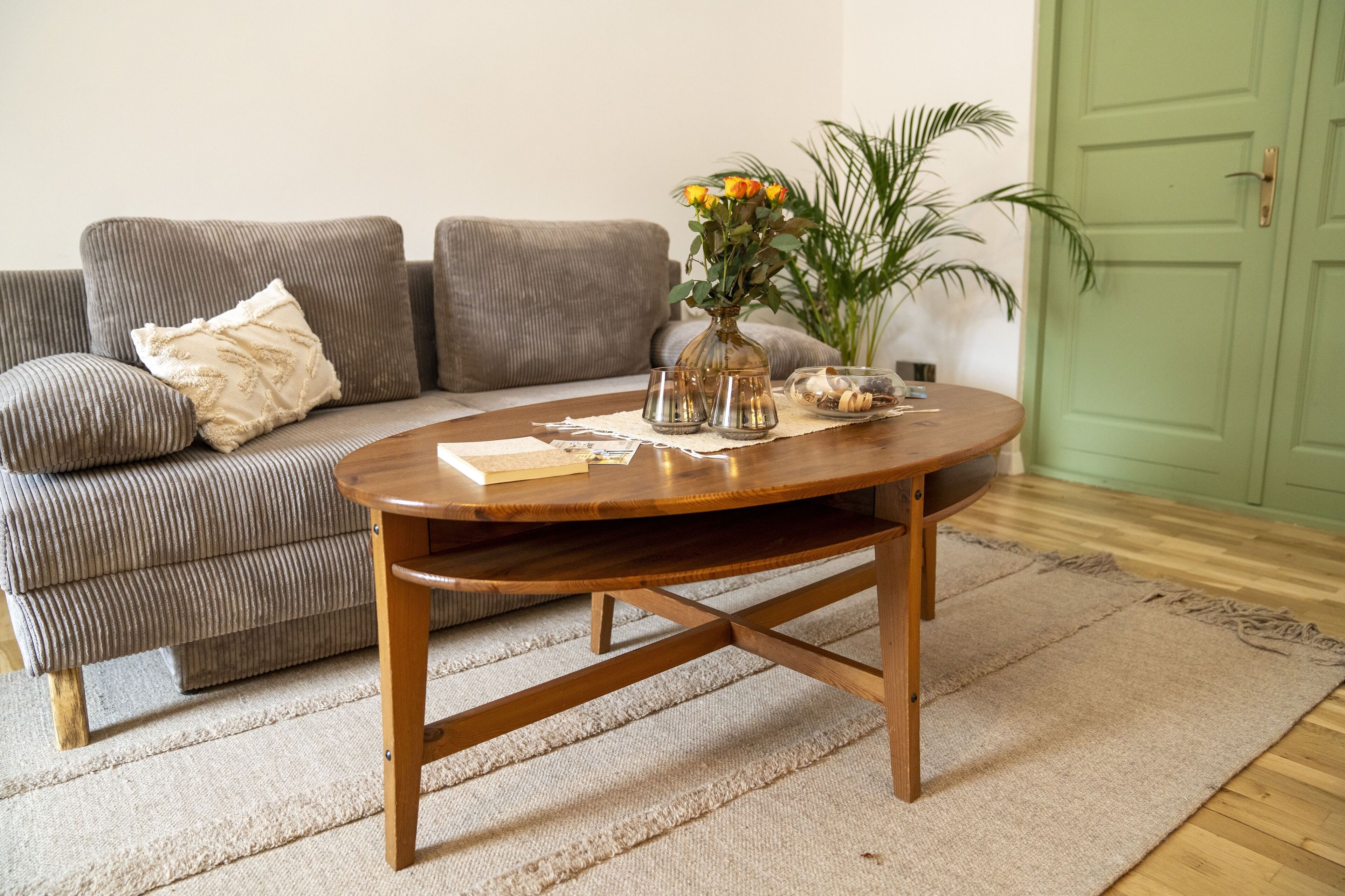 A living room with a wooden coffee table, a grey sofa, a green door, and a plant.