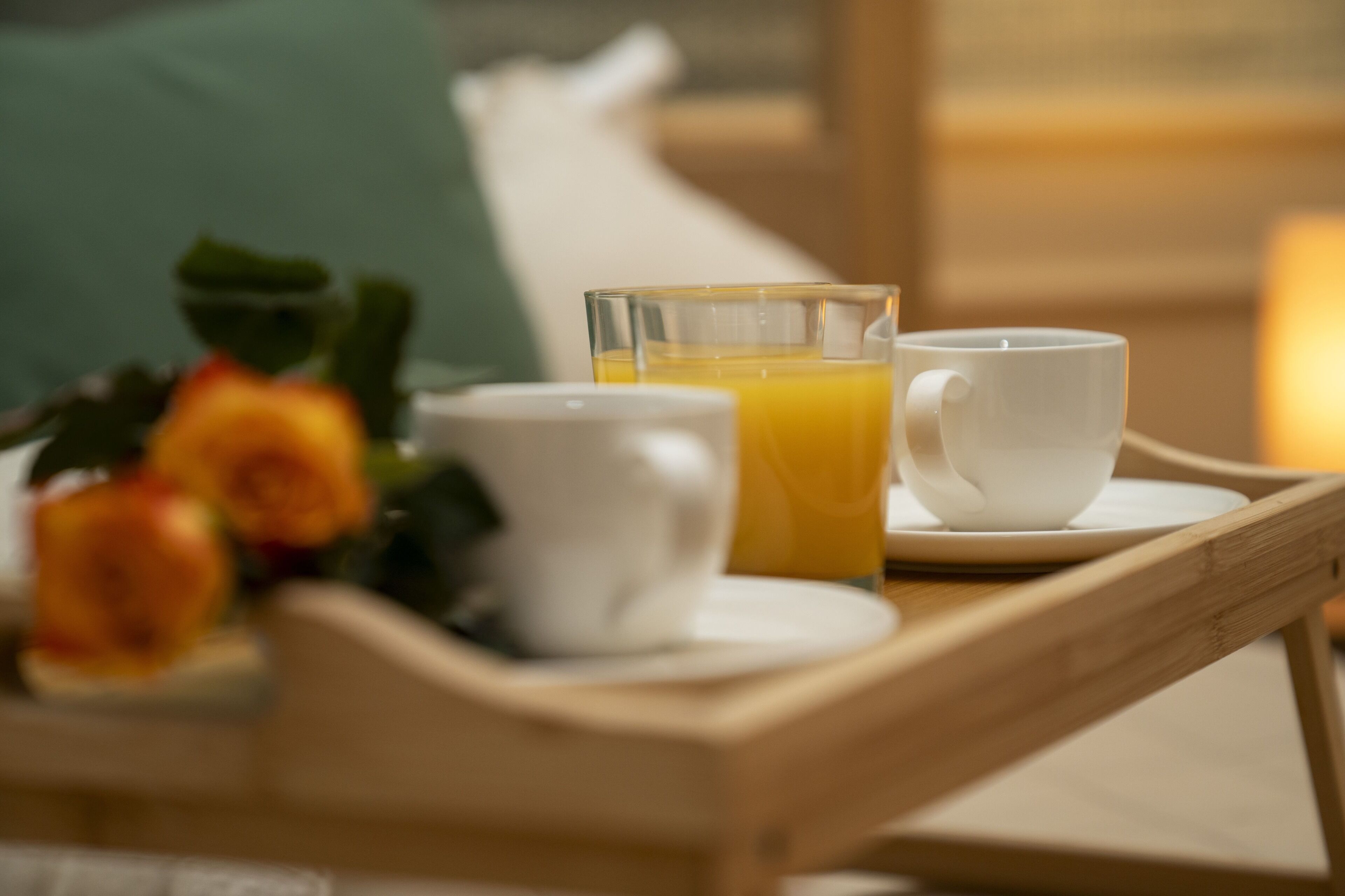 Un plateau avec un verre de jus d’orange, une tasse blanche et une soucoupe blanche, posés sur une table en bois.
