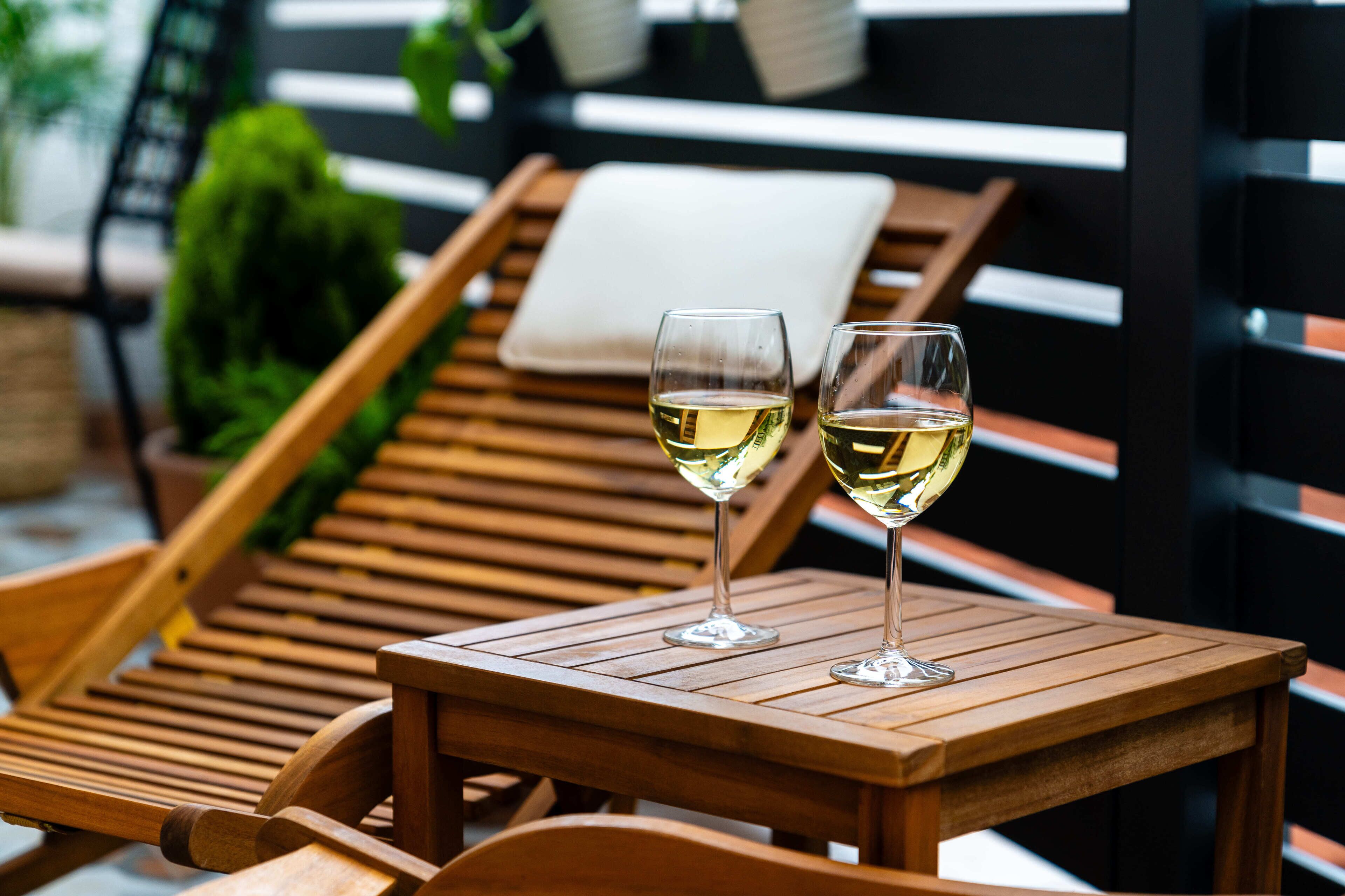 Dos copas de vino blanco sobre una mesa de madera, con un banco al fondo.