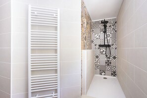 Un espace douche avec une baignoire blanche, un porte-serviettes blanc et des carreaux décoratifs sur les murs.