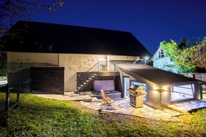 Une maison moderne avec une façade en pierre, une terrasse en bois et un espace barbecue.