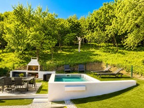 A pool with a barbecue area, lounge chairs, and a grassy hill with trees. - Luxury forest home with private pool, jacuzzi, sauna and playground (Vrbovsko)