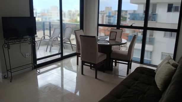 Una sala de estar moderna con una mesa de comedor de vidrio, sillas, un sofá y un televisor sobre un mueble.