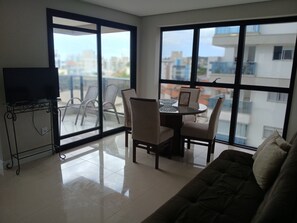A modern living room with a glass dining table, chairs, a sofa, and a TV on a stand. - Apartment on Palmas Beach (Governador Celso Ramos)