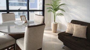 Una sala de estar moderna con una mesa de comedor de vidrio, sillas color beige, un sofá marrón oscuro y una planta grande en maceta.