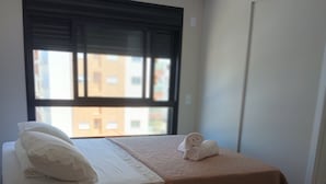 Una habitación de hotel con una cama, una mesita de noche, una ventana y una puerta.