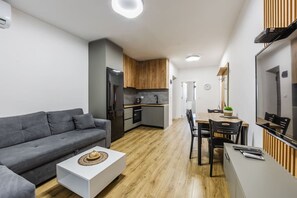 A modern living room with a grey sofa, a white coffee table, and a dining area with a wooden table and chairs. - City Center Apartment Cozy 1BR With Patio (Tirana)