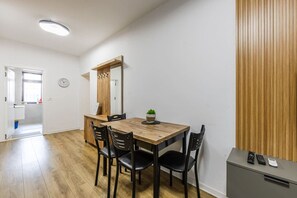 Un coin repas avec une table en bois, quatre chaises, une petite plante en pot, une horloge au mur et un panneau en bois sur le mur.